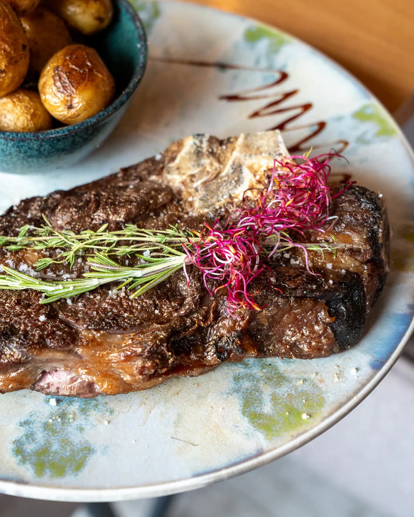 Côte de bœuf à l'os halal grillée au charbon de bois, romarin et pousses, servie avec un bol de pommes grenailles